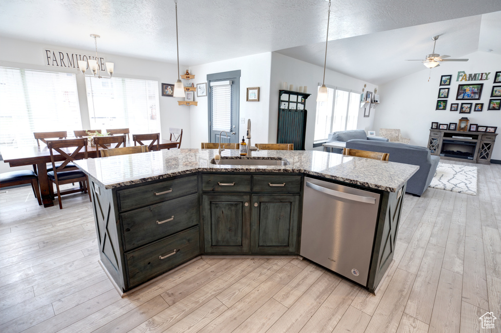 Kitchen featuring stainless steel dishwasher, a sink, a ceiling fan, light wood-type flooring, and light stone counters