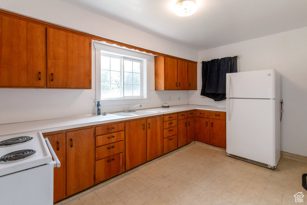 Kitchen with white appliances, a sink, light countertops, and brown cabinetry