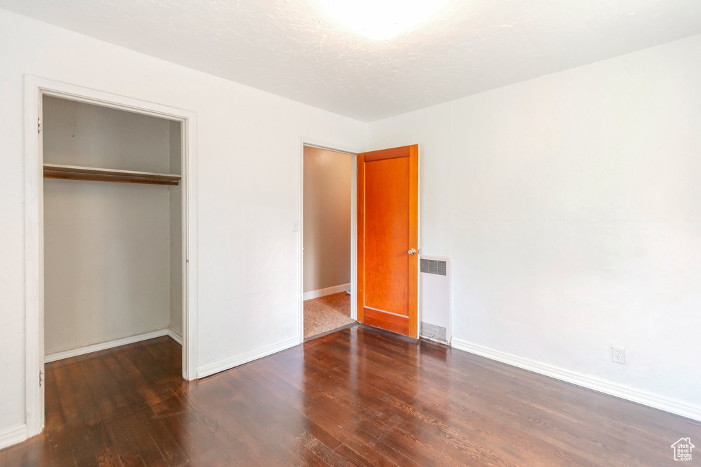 Unfurnished bedroom featuring radiator, wood finished floors, baseboards, and a closet