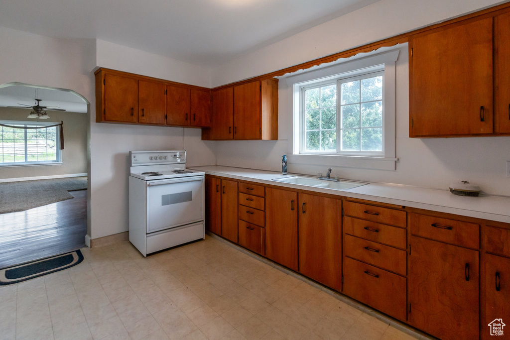 Kitchen with white range with electric stovetop, brown cabinetry, light countertops, and a ceiling fan