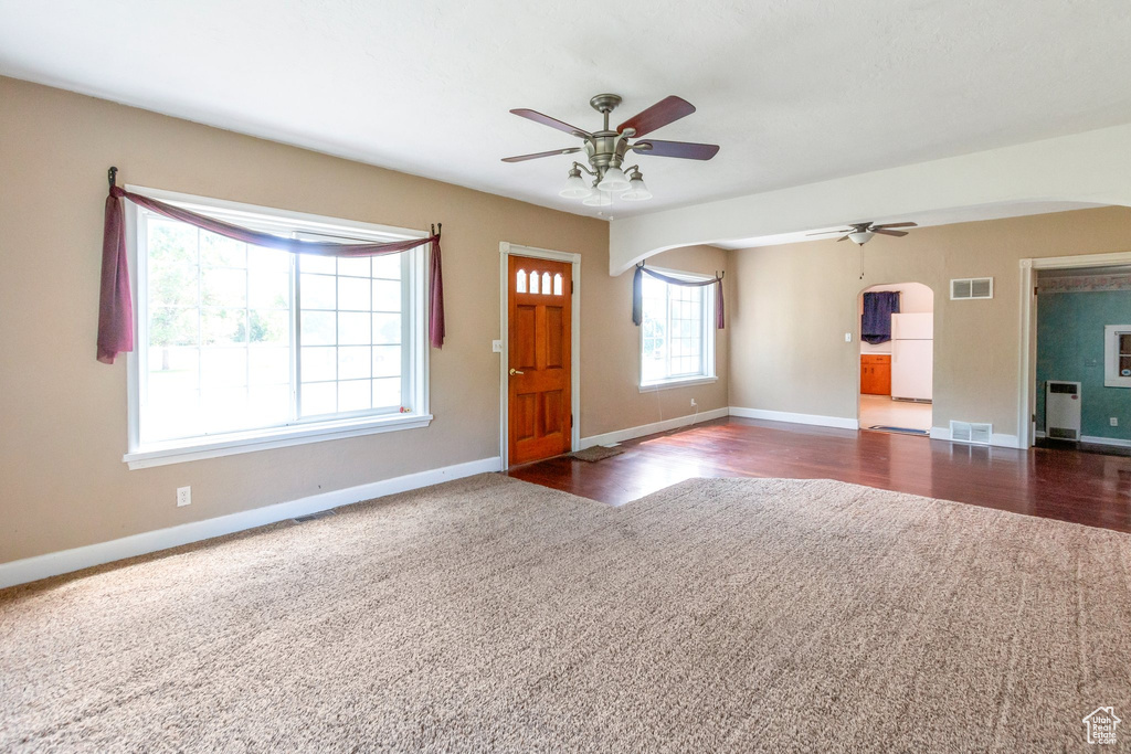 Carpeted foyer featuring arched walkways, a ceiling fan, baseboards, and wood finished floors