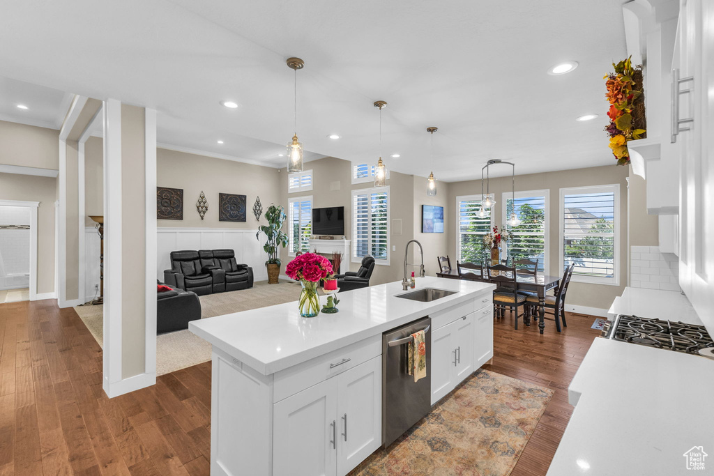Kitchen with stainless steel dishwasher, a sink, light countertops, white cabinets, and open floor plan