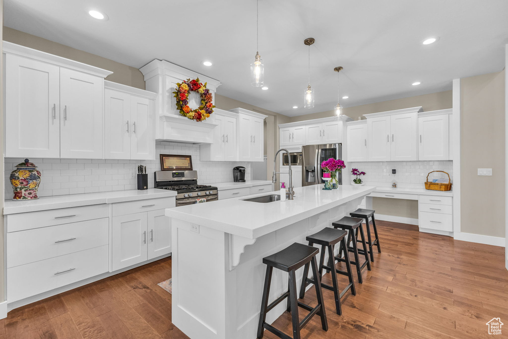 Kitchen with stainless steel appliances, a sink, decorative backsplash, a kitchen breakfast bar, and white cabinetry