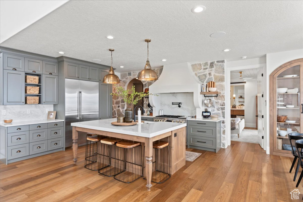 Kitchen with gray cabinetry, open shelves, stainless steel built in fridge, custom range hood, and tasteful backsplash