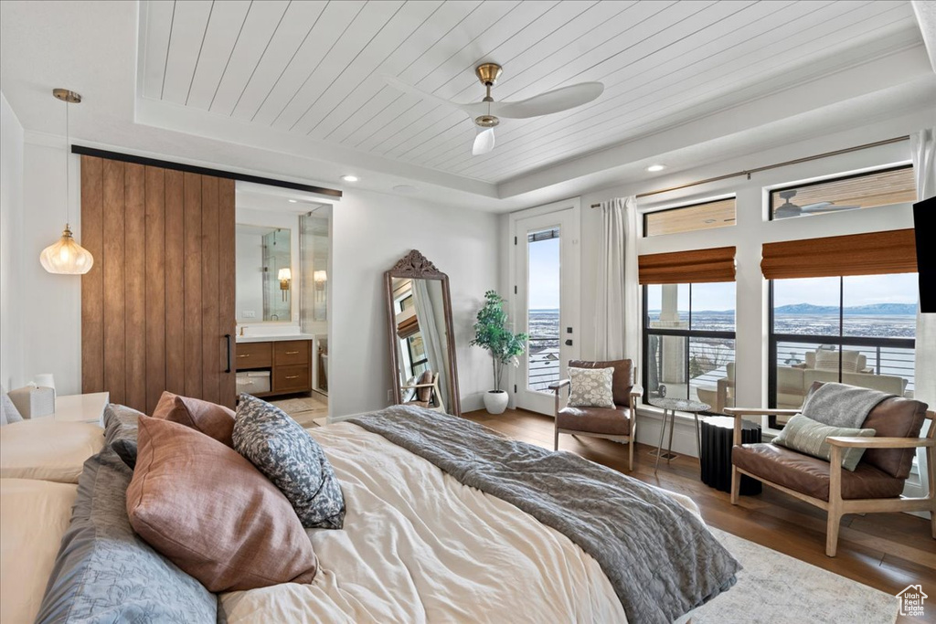 Bedroom featuring a raised ceiling, light wood-style flooring, wood ceiling, and connected bathroom