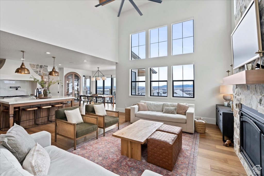 Living room featuring a fireplace, light wood finished floors, a towering ceiling, a ceiling fan, and baseboards