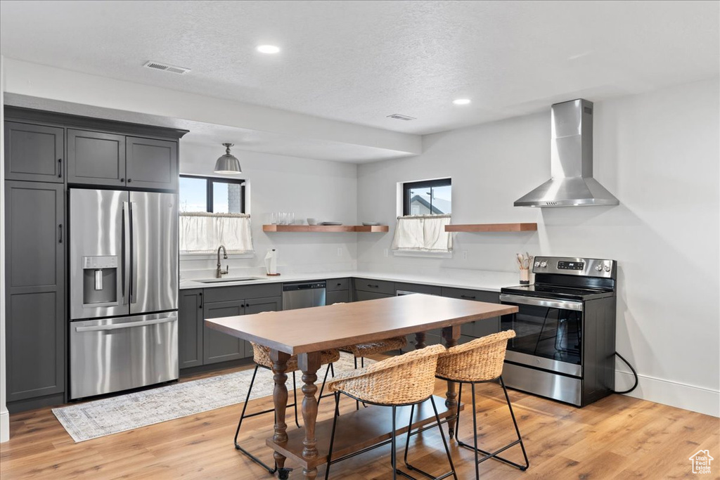 Kitchen with stainless steel appliances, wall chimney exhaust hood, open shelves, a sink, and plenty of natural light