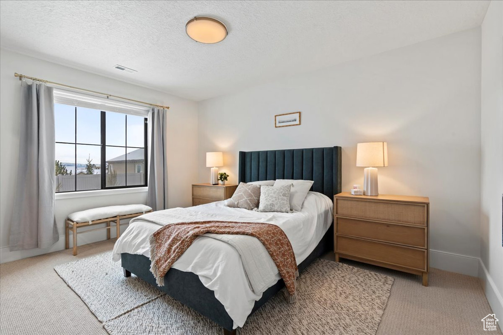 Bedroom with light carpet, a textured ceiling, and baseboards