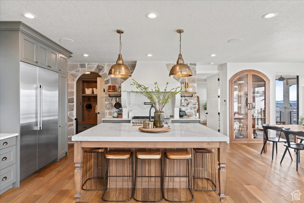Kitchen featuring built in refrigerator, gray cabinets, light wood-type flooring, a textured ceiling, and arched walkways