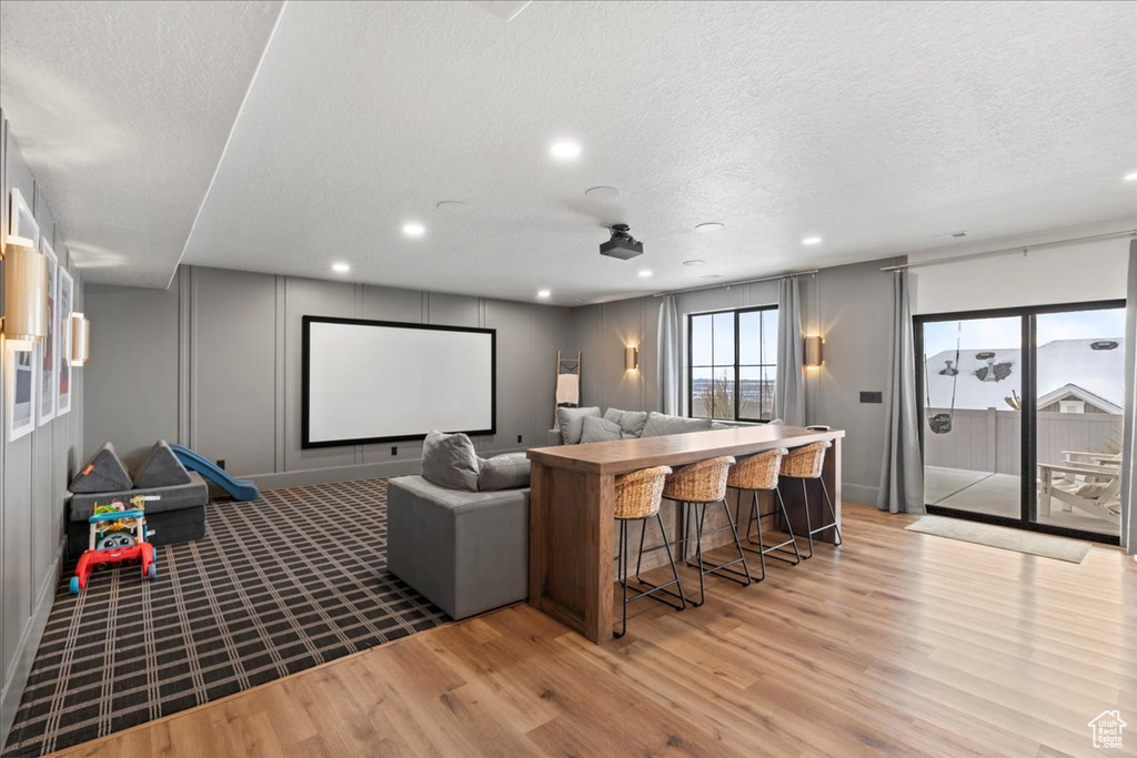 Cinema with light wood-type flooring, a textured ceiling, recessed lighting, a decorative wall, and baseboards