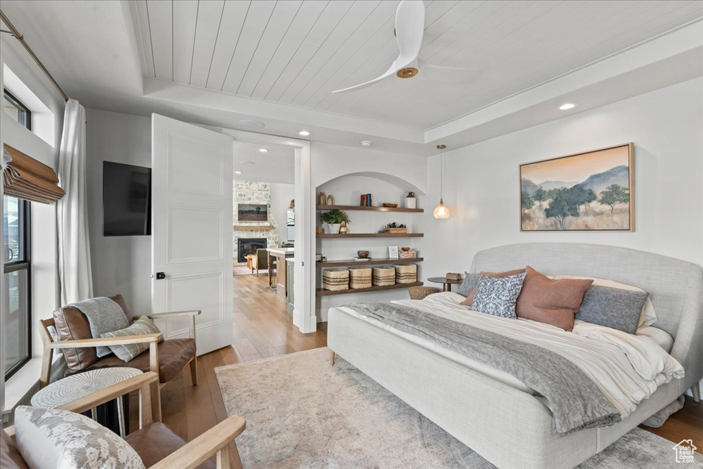 Bedroom with light wood-style flooring, a tray ceiling, a glass covered fireplace, recessed lighting, and a ceiling fan