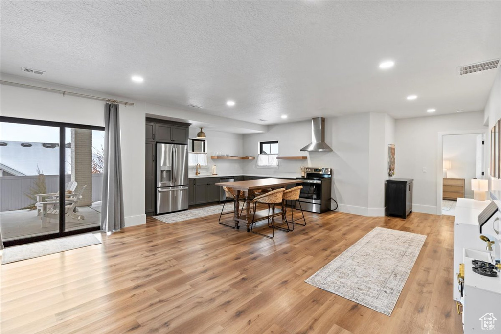 Kitchen featuring stainless steel appliances, wall chimney exhaust hood, gray cabinetry, light wood-style flooring, and open shelves