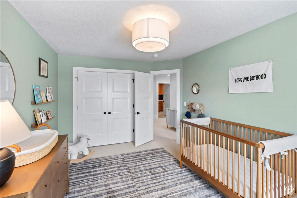 Bedroom with a closet, carpet floors, a nursery area, and a textured ceiling