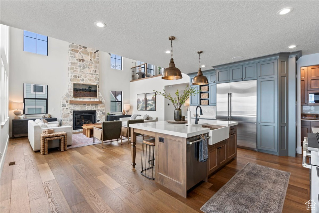 Kitchen featuring appliances with stainless steel finishes, a textured ceiling, light countertops, a fireplace, and a center island with sink