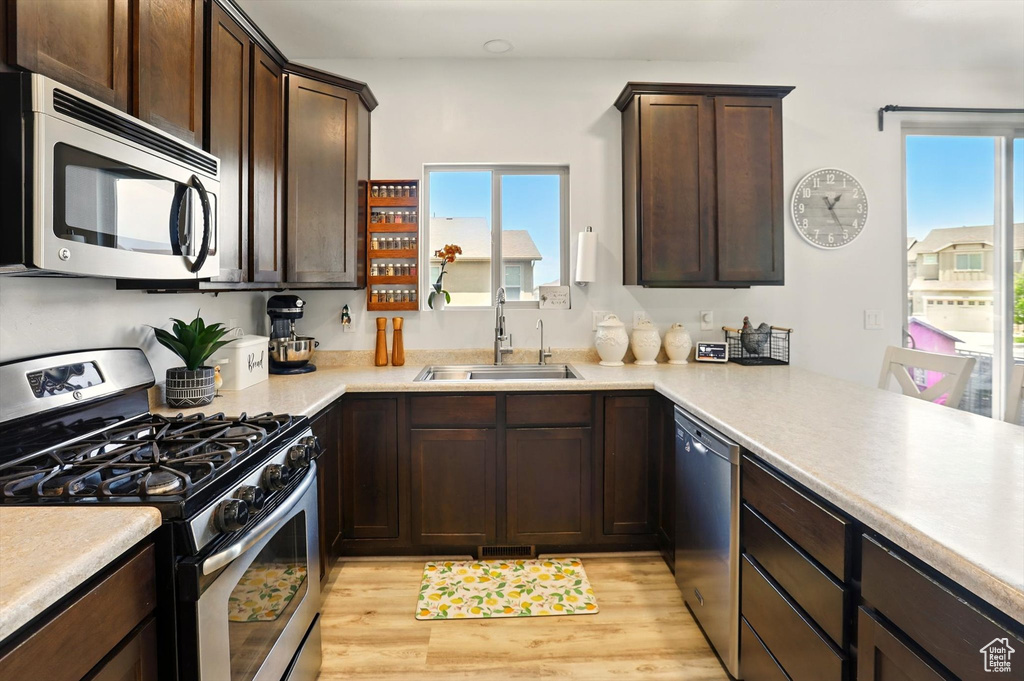 Kitchen featuring stainless steel appliances, a sink, dark brown cabinets, and light countertops