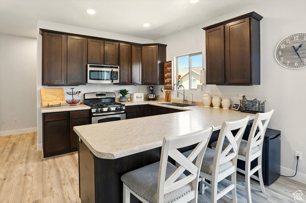 Kitchen featuring stainless steel appliances, light countertops, dark brown cabinets, a peninsula, and a kitchen breakfast bar