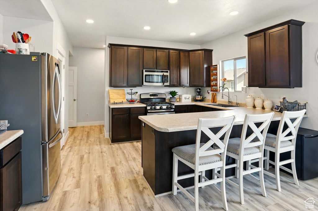 Kitchen with appliances with stainless steel finishes, a sink, dark brown cabinetry, a peninsula, and recessed lighting