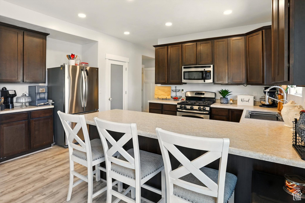 Kitchen with stainless steel appliances, a sink, dark brown cabinets, light countertops, and light wood-type flooring