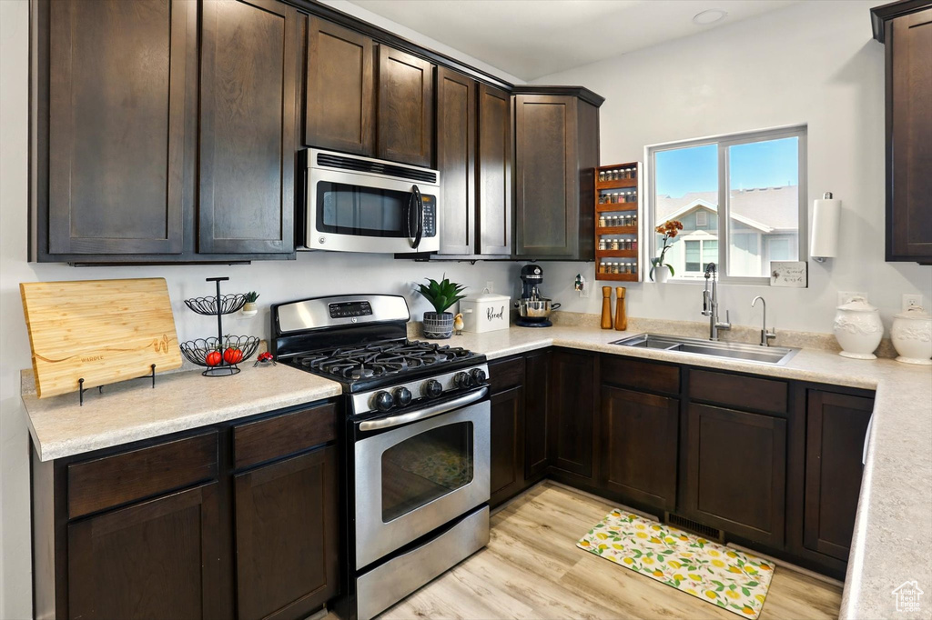 Kitchen with appliances with stainless steel finishes, a sink, dark brown cabinets, and light wood finished floors