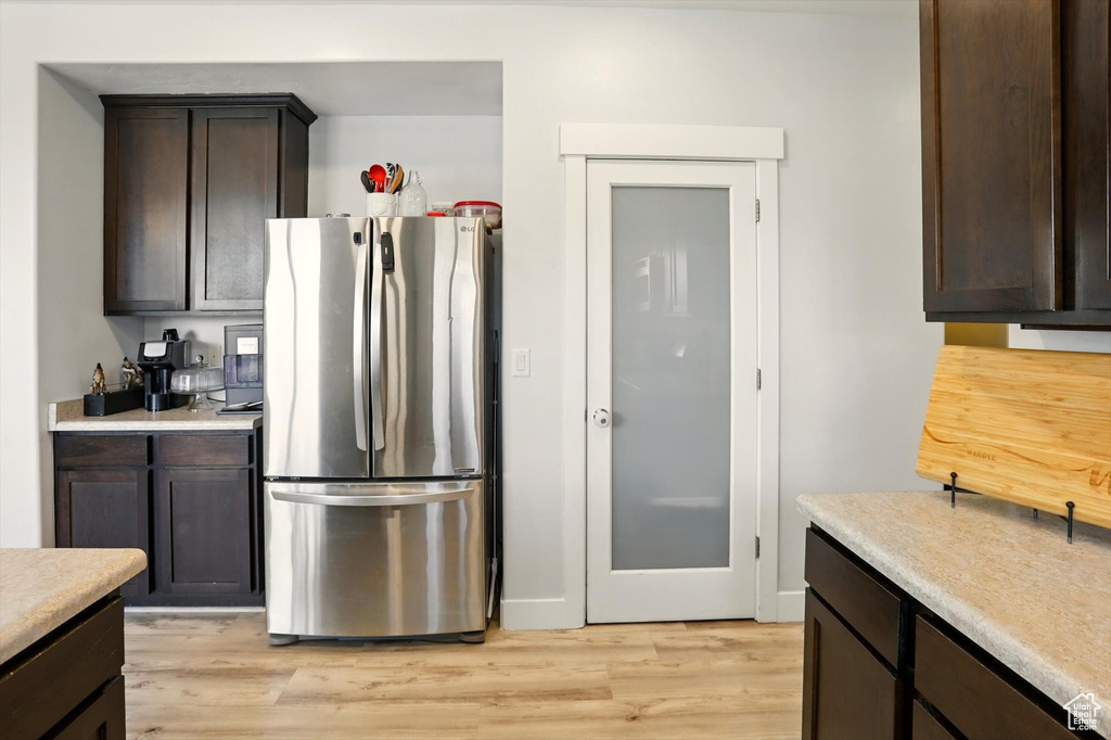 Kitchen featuring freestanding refrigerator, dark brown cabinetry, light wood-type flooring, and light countertops