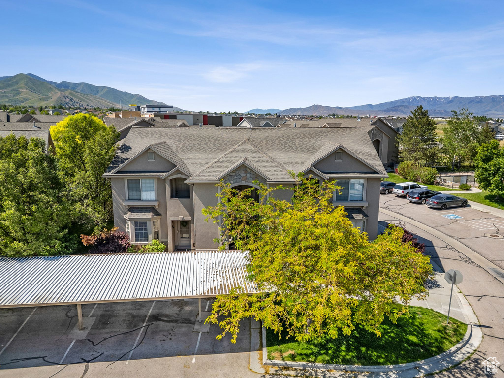 View of front facade featuring uncovered parking, a mountain view, a shingled roof, and stucco siding
