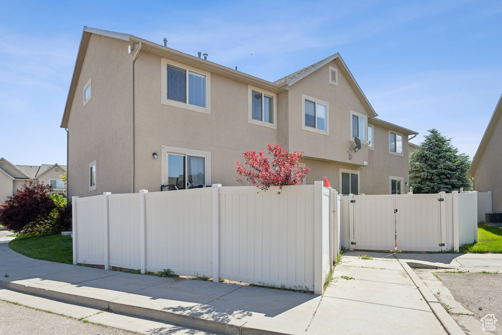 View of side of home with a gate, stucco siding, and central AC unit