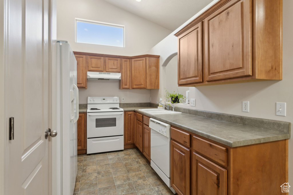 Kitchen featuring white appliances, under cabinet range hood, a sink, brown cabinetry, and high vaulted ceiling