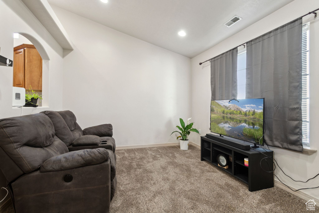 Carpeted living room featuring lofted ceiling, arched walkways, baseboards, and recessed lighting