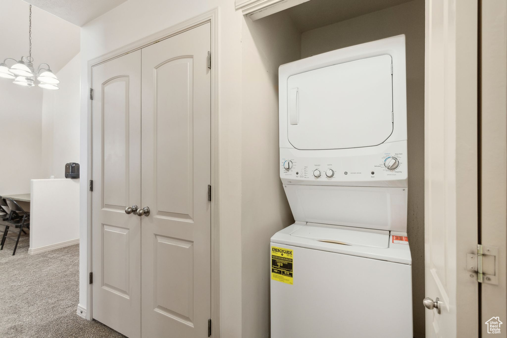 Laundry area with stacked washer and clothes dryer, carpet flooring, and a chandelier
