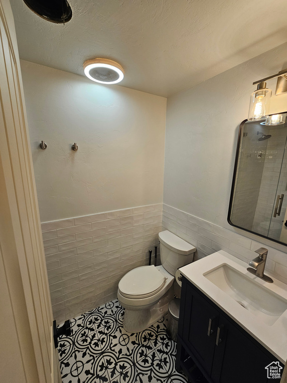 Bathroom with tile walls, toilet, wainscoting, tile patterned flooring, and vanity