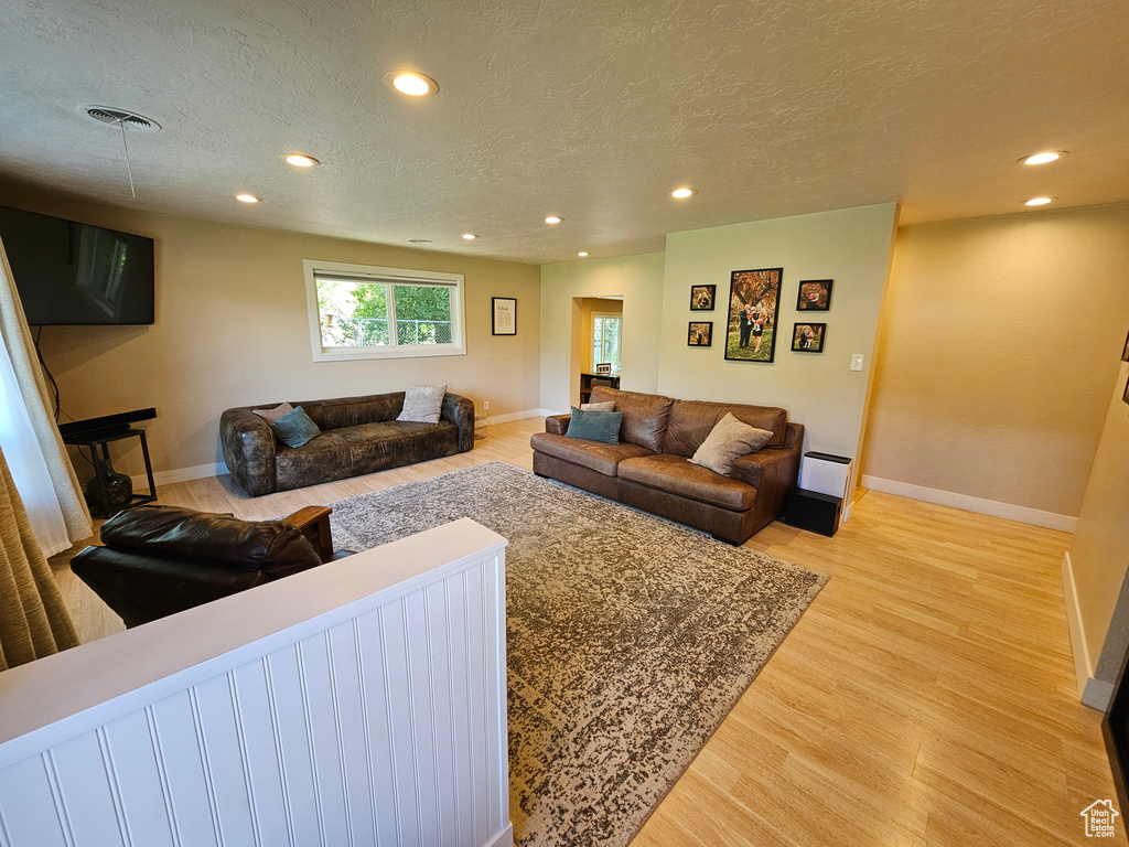 Living room with recessed lighting, light wood-type flooring, baseboards, and a textured ceiling