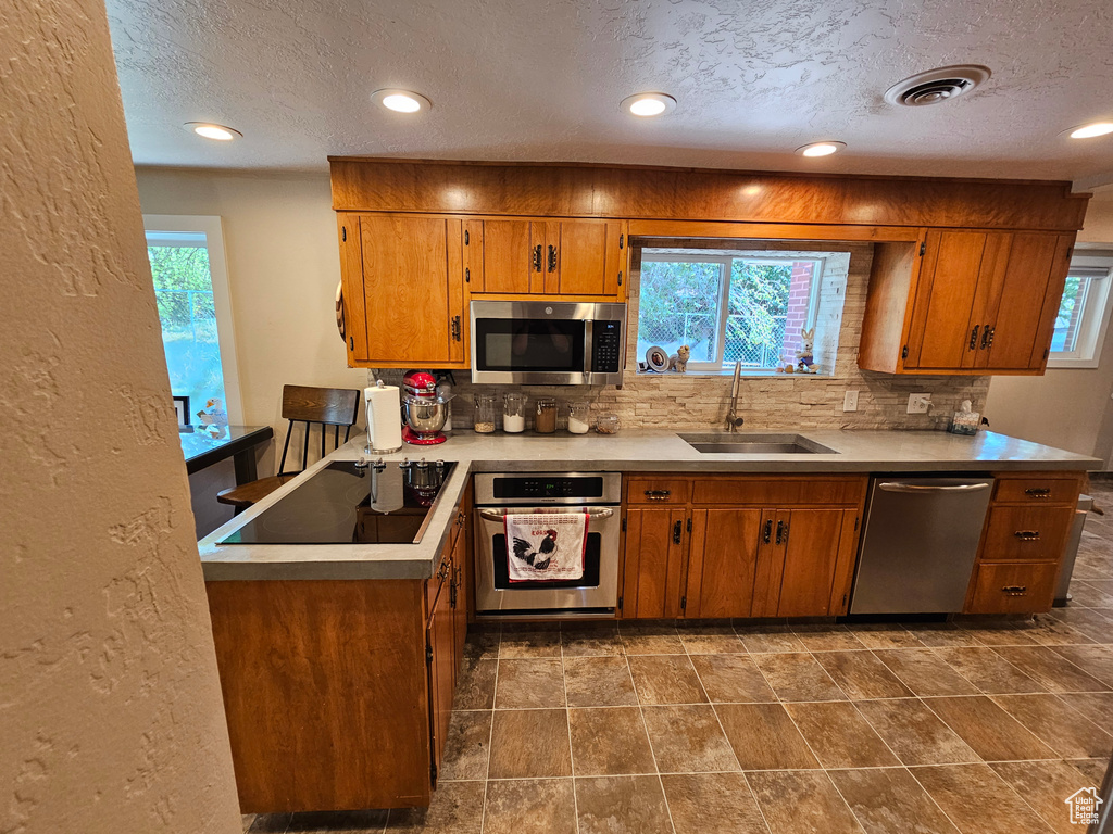 Kitchen with stainless steel appliances, a sink, brown cabinets, tasteful backsplash, and a textured ceiling