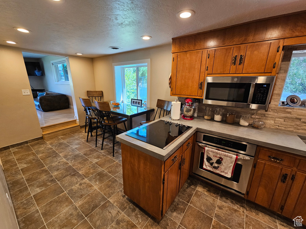 Kitchen featuring stainless steel appliances, decorative backsplash, brown cabinets, a peninsula, and light countertops