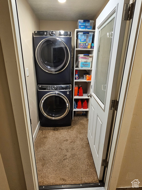 Laundry area featuring stacked washing machine and dryer and carpet flooring