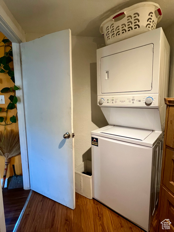 Washroom with stacked washer / drying machine and wood finished floors