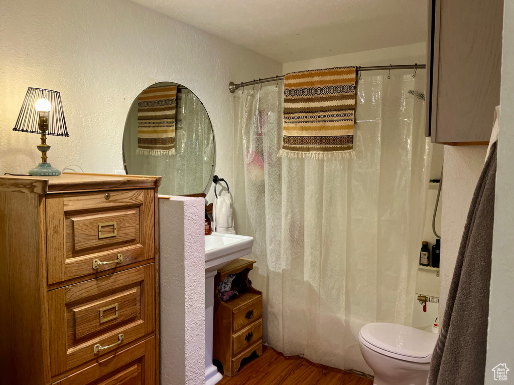 Full bath with wood finished floors, a textured wall, toilet, and shower / bath combo