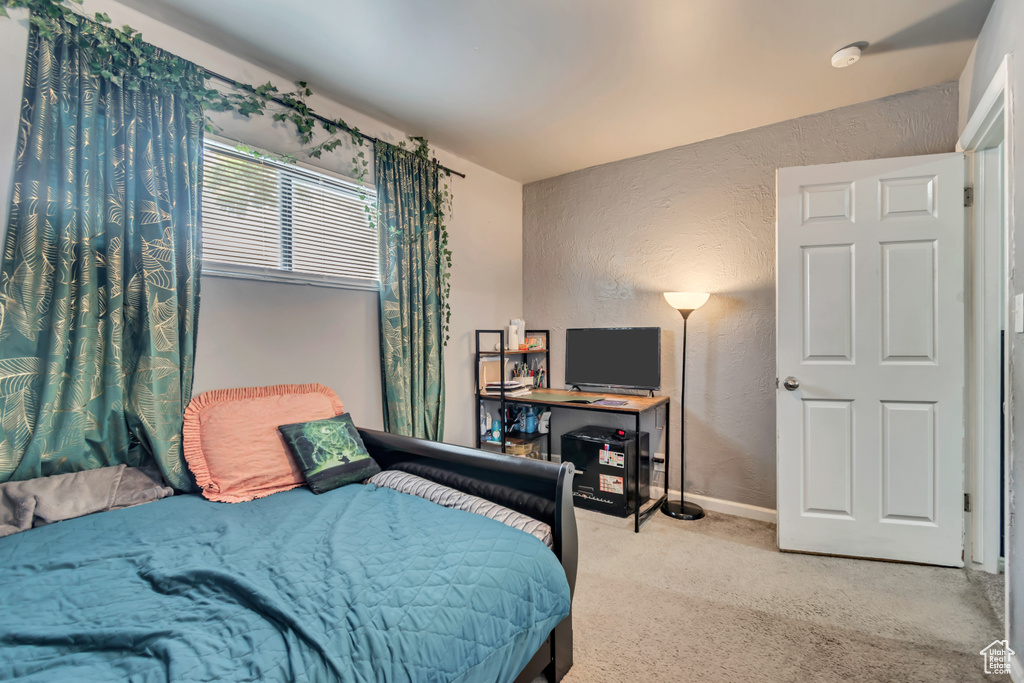 Bedroom with light carpet, a textured wall, and baseboards