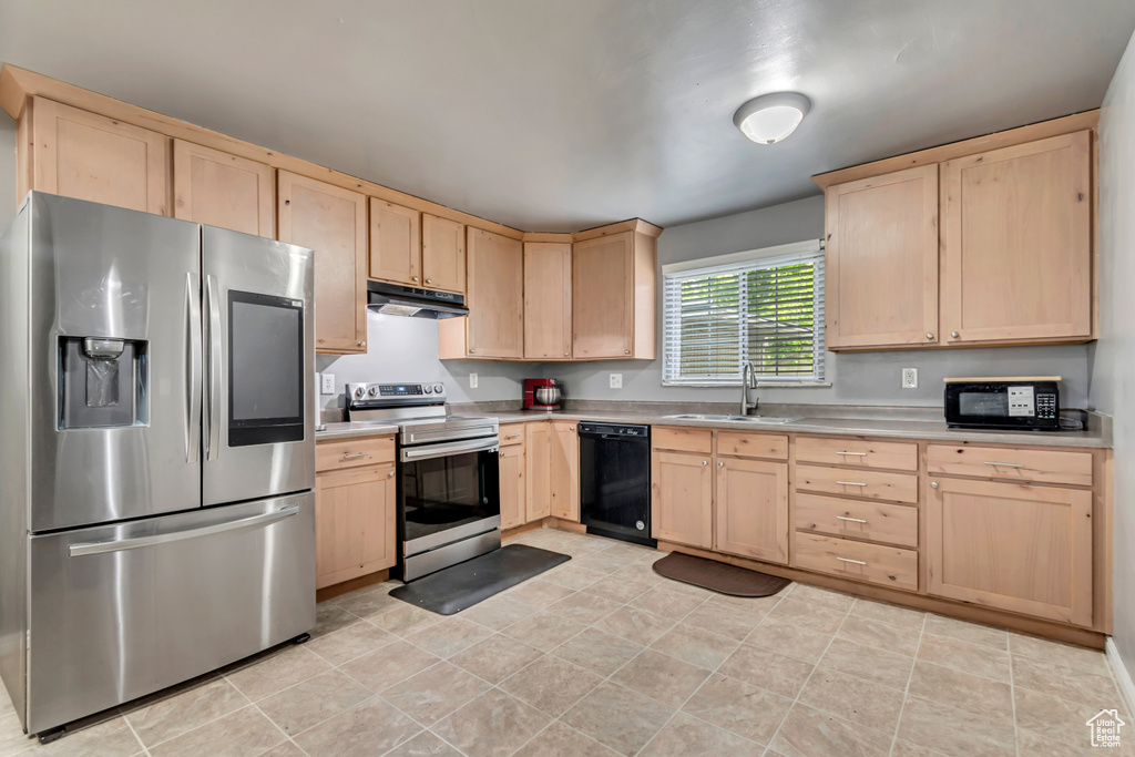 Kitchen with black appliances, light brown cabinetry, a sink, and light countertops