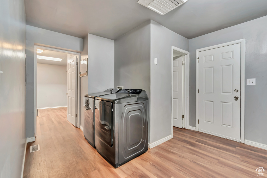Washroom with washing machine and dryer, light wood finished floors, and baseboards