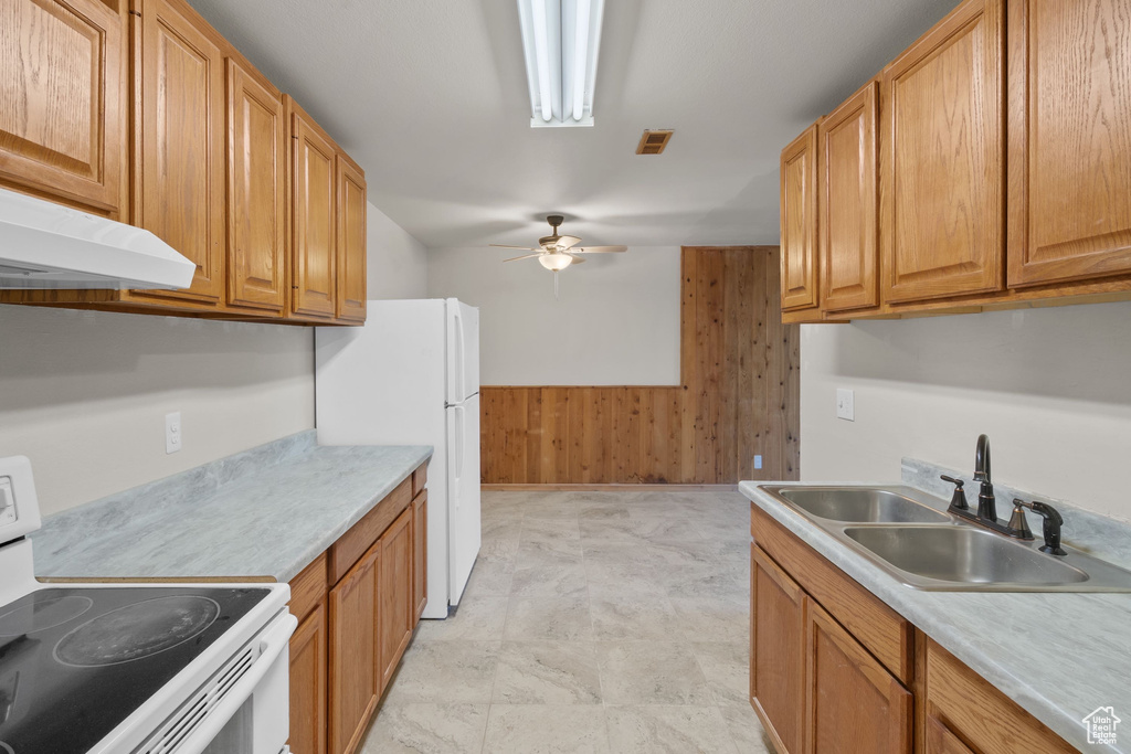 Kitchen featuring white appliances, a sink, wooden walls, a ceiling fan, and under cabinet range hood