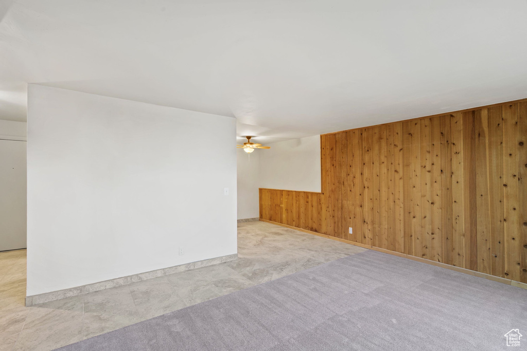 Carpeted spare room featuring wooden walls, ceiling fan, and baseboards