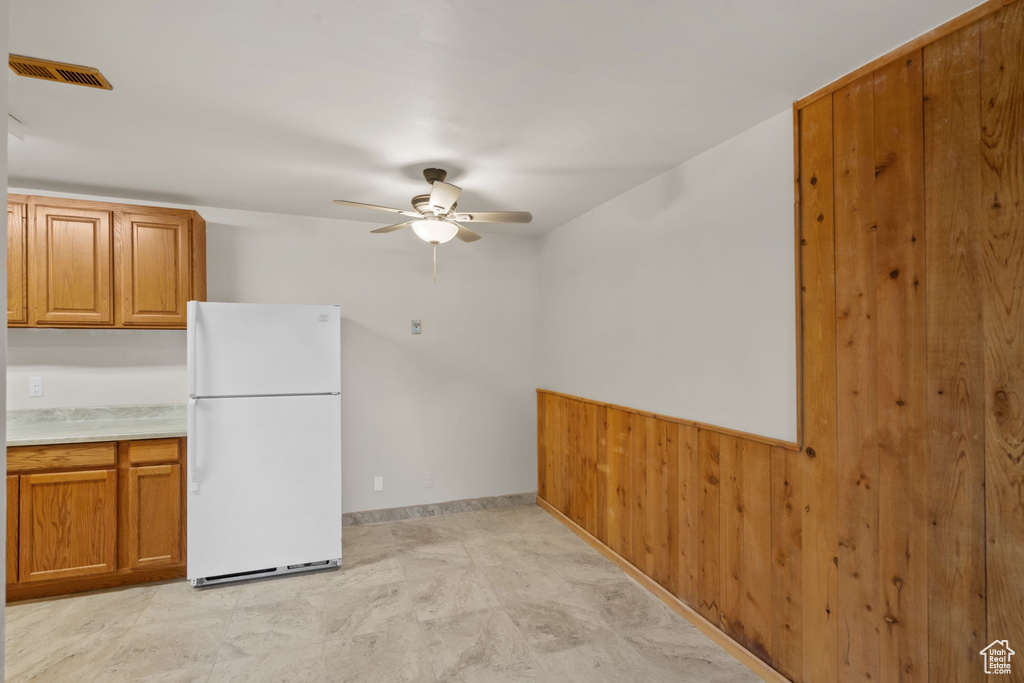 Kitchen featuring freestanding refrigerator, brown cabinetry, a ceiling fan, light countertops, and baseboards