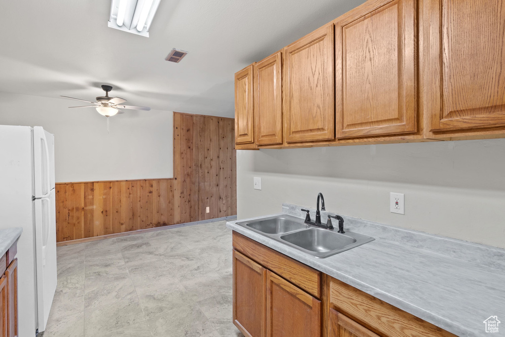 Kitchen with freestanding refrigerator, a sink, wooden walls, light countertops, and a ceiling fan