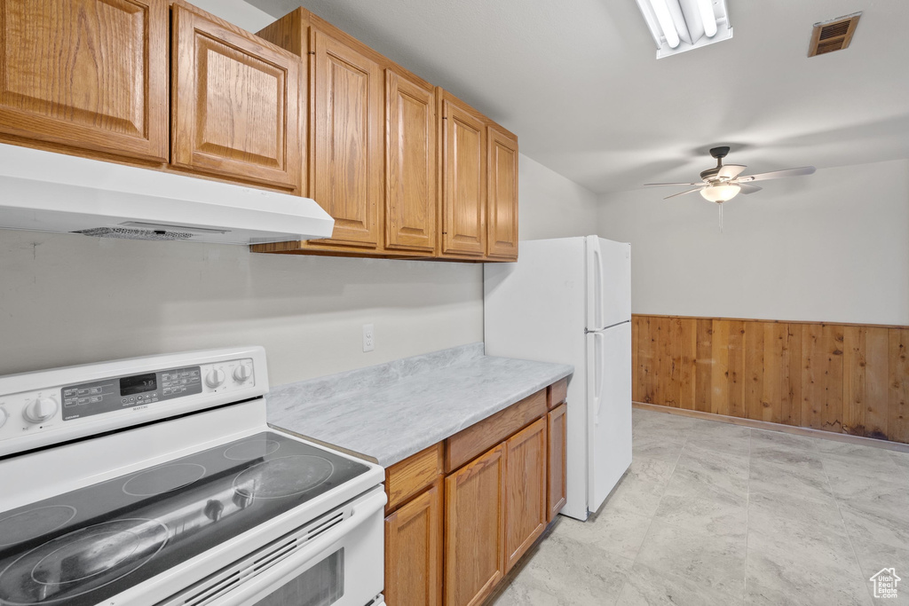 Kitchen featuring white appliances, under cabinet range hood, light countertops, ceiling fan, and a wainscoted wall