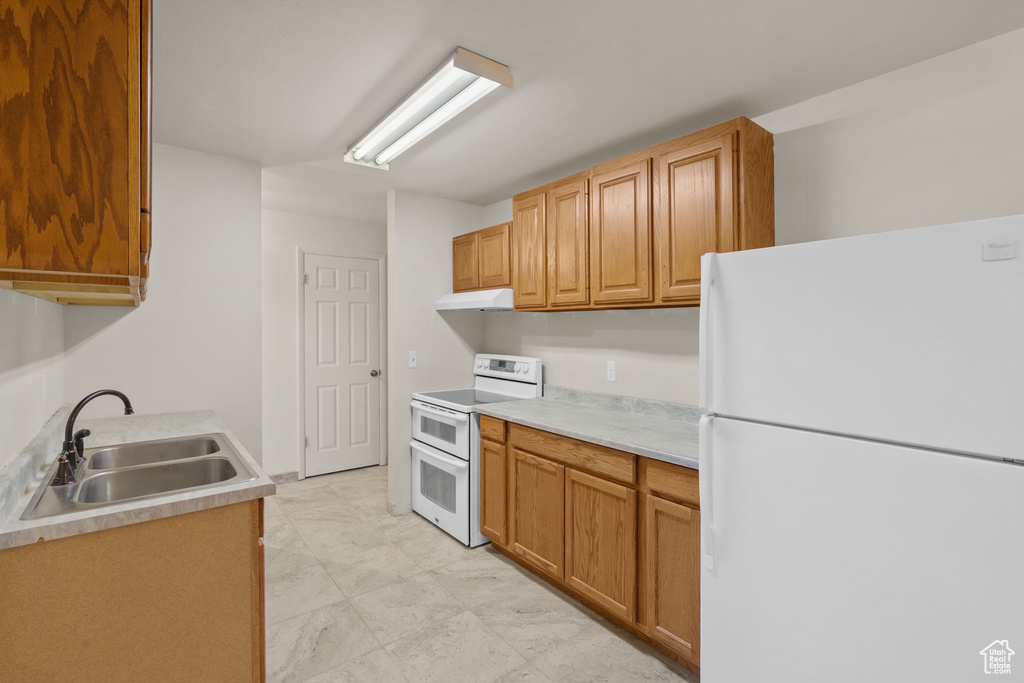 Kitchen featuring white appliances, a sink, under cabinet range hood, and light countertops