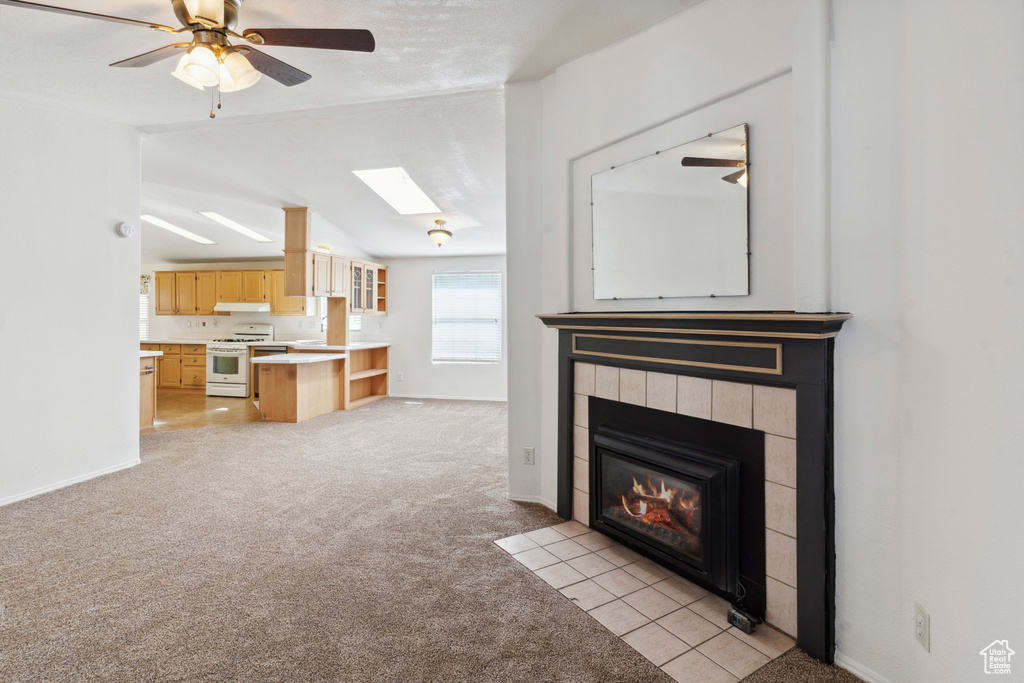 Unfurnished living room with light colored carpet, a skylight, a fireplace, baseboards, and vaulted ceiling