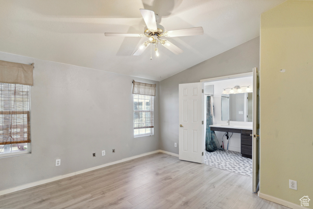 Unfurnished bedroom with lofted ceiling, wood finished floors, a sink, ensuite bath, and baseboards