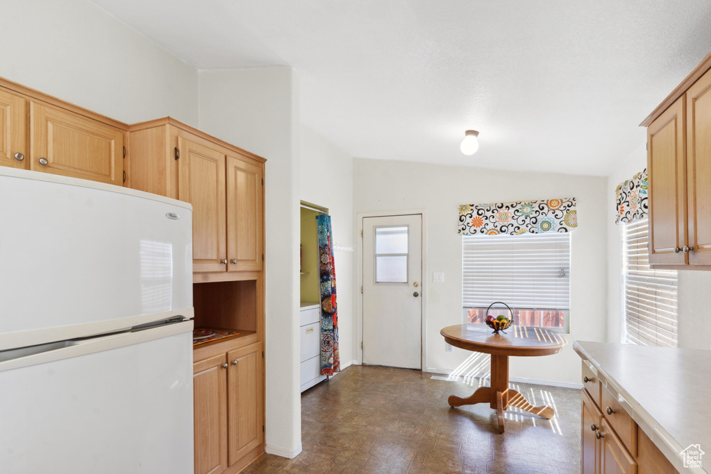Kitchen featuring freestanding refrigerator, lofted ceiling, healthy amount of natural light, light brown cabinets, and dark floors