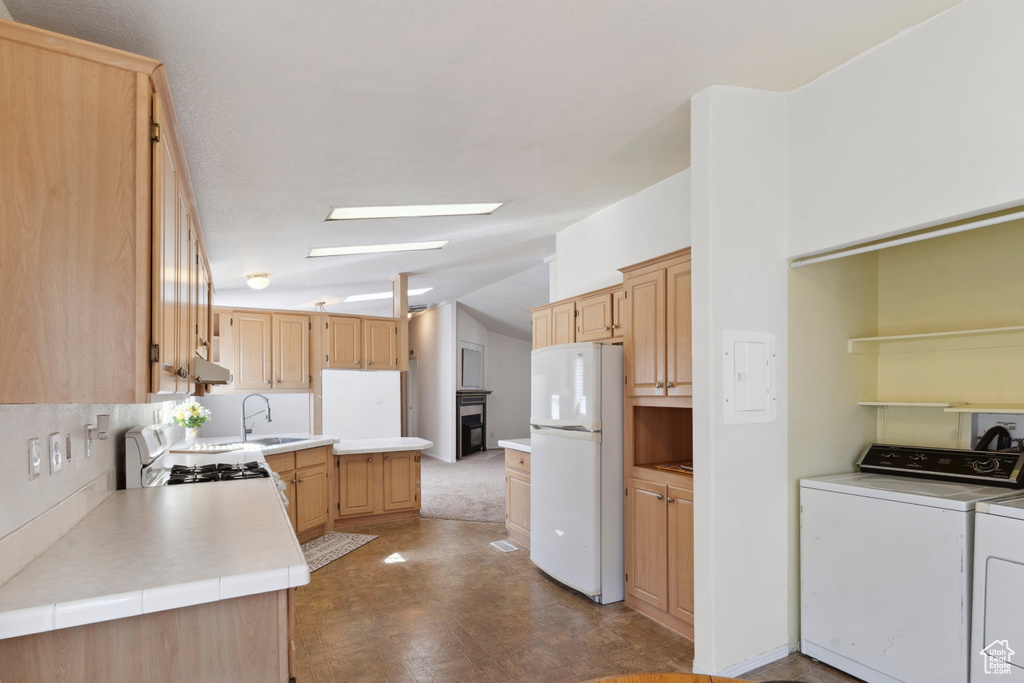 Kitchen with white appliances, separate washer and dryer, vaulted ceiling, light brown cabinetry, and light countertops