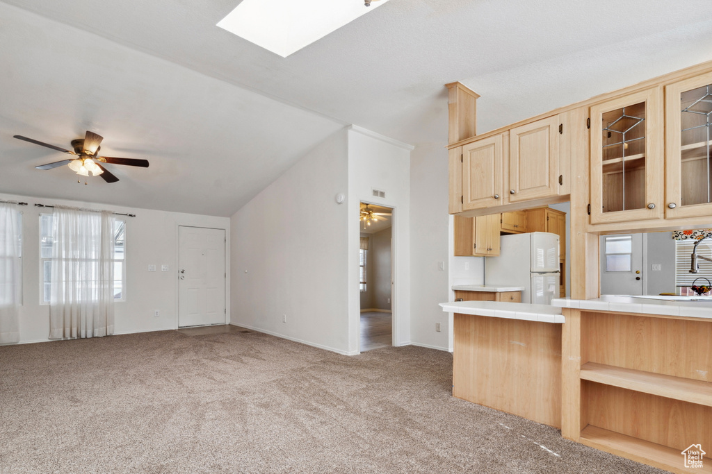 Kitchen with freestanding refrigerator, ceiling fan, light colored carpet, tile countertops, and light brown cabinets
